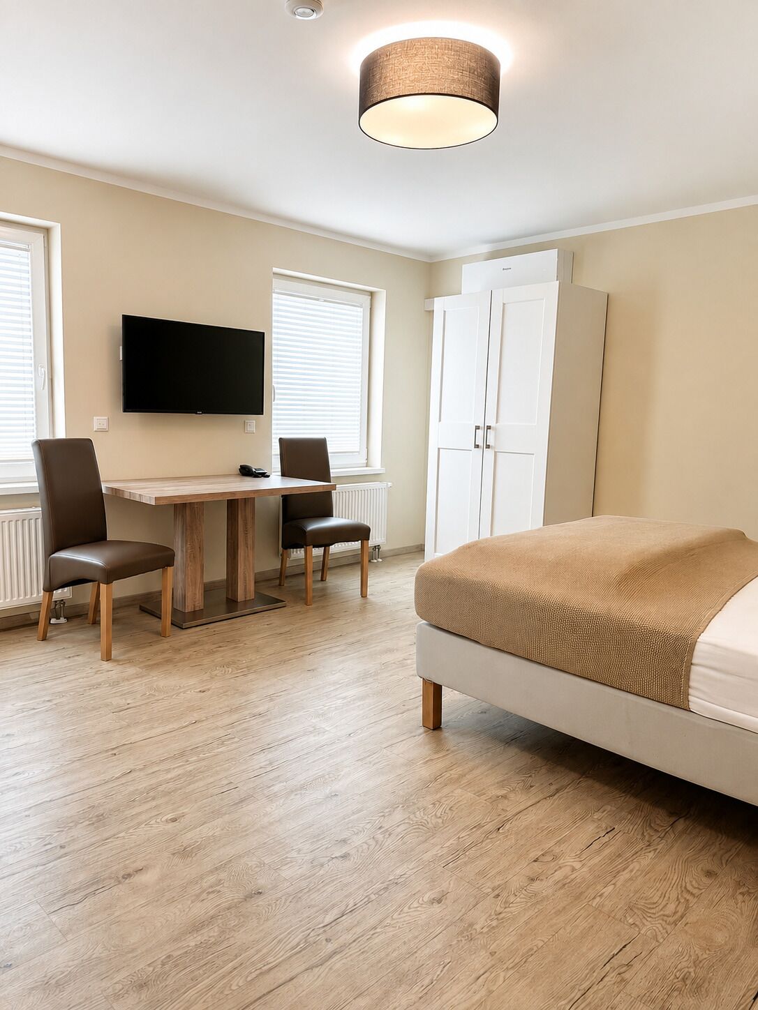 A modern bedroom with a bed, a desk, chairs, a television, and a wardrobe.