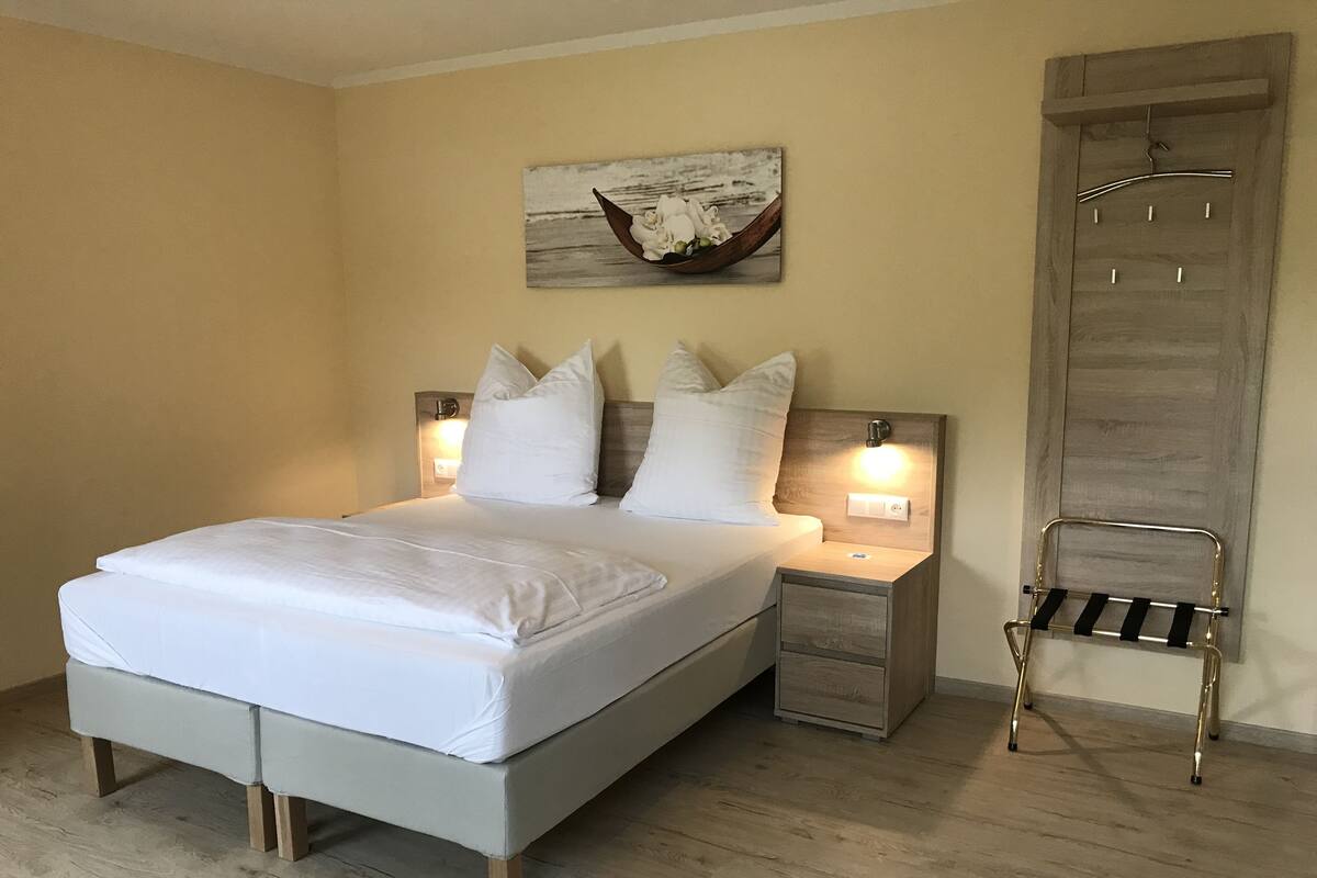 A neatly made bed with white linens, a wooden headboard, bedside tables with lamps, and a wall-mounted towel rack.