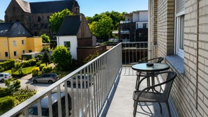 A balcony with a table and chairs, overlooking a street with cars and buildings, including a church. - Hotel Select Suites & Aparts (Moenchengladbach)