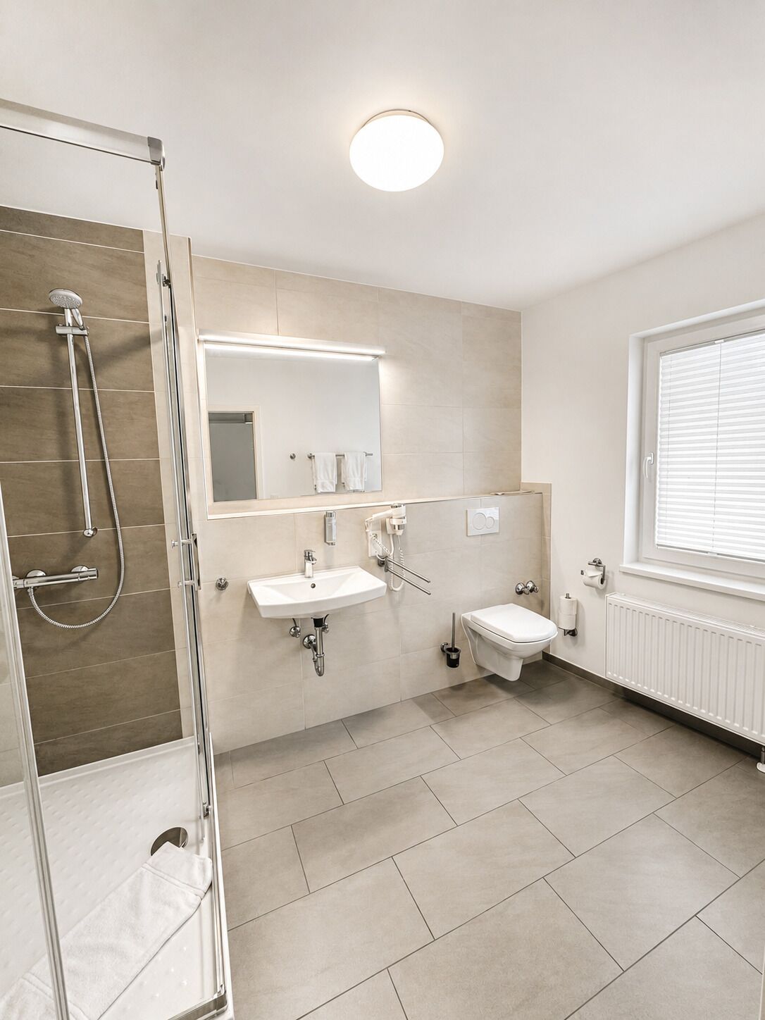 Ein modernes Badezimmer mit Duschkabine aus Glas, Waschbecken, Toilette und großem Spiegel.