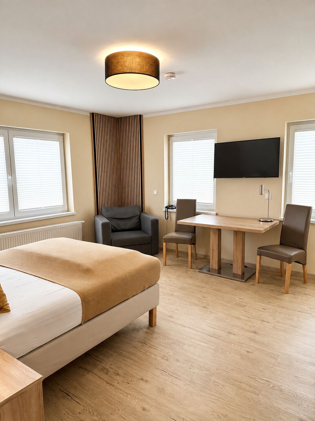 Een hotelkamer met een bed, een bureau, twee stoelen, een televisietoestel en een raam met zonwering.