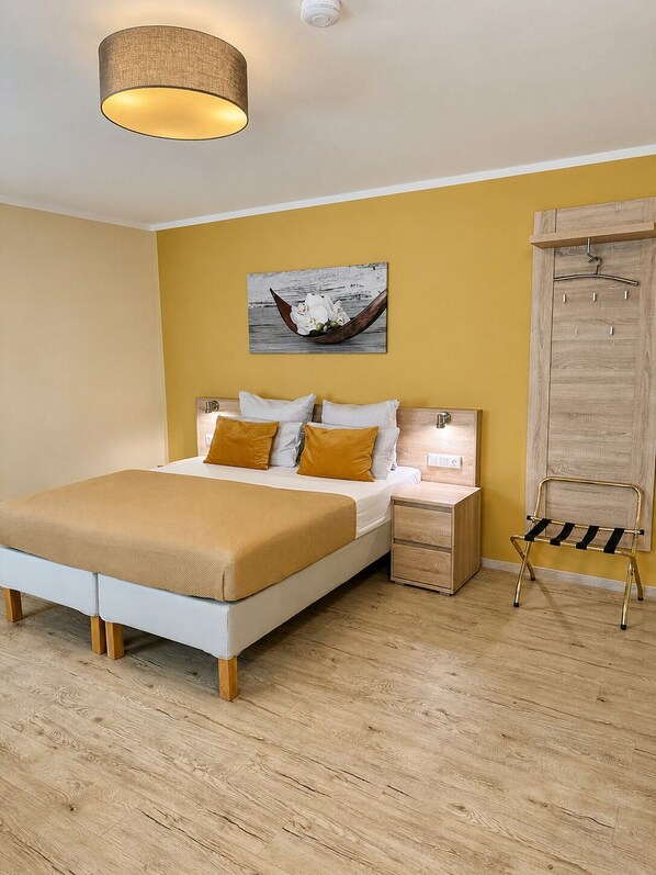 A bedroom with a bed, bedside tables, a hanging light fixture, a wooden wardrobe, and a wall-mounted artwork. - Hotel Select Suites & Aparts (Moenchengladbach)