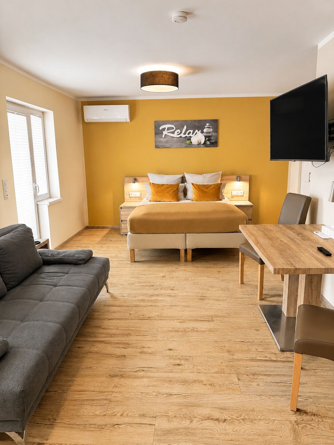 Une chambre d’hôtel comprenant un lit, un canapé, une table à manger en bois, un téléviseur et une œuvre d’art accrochée au mur.