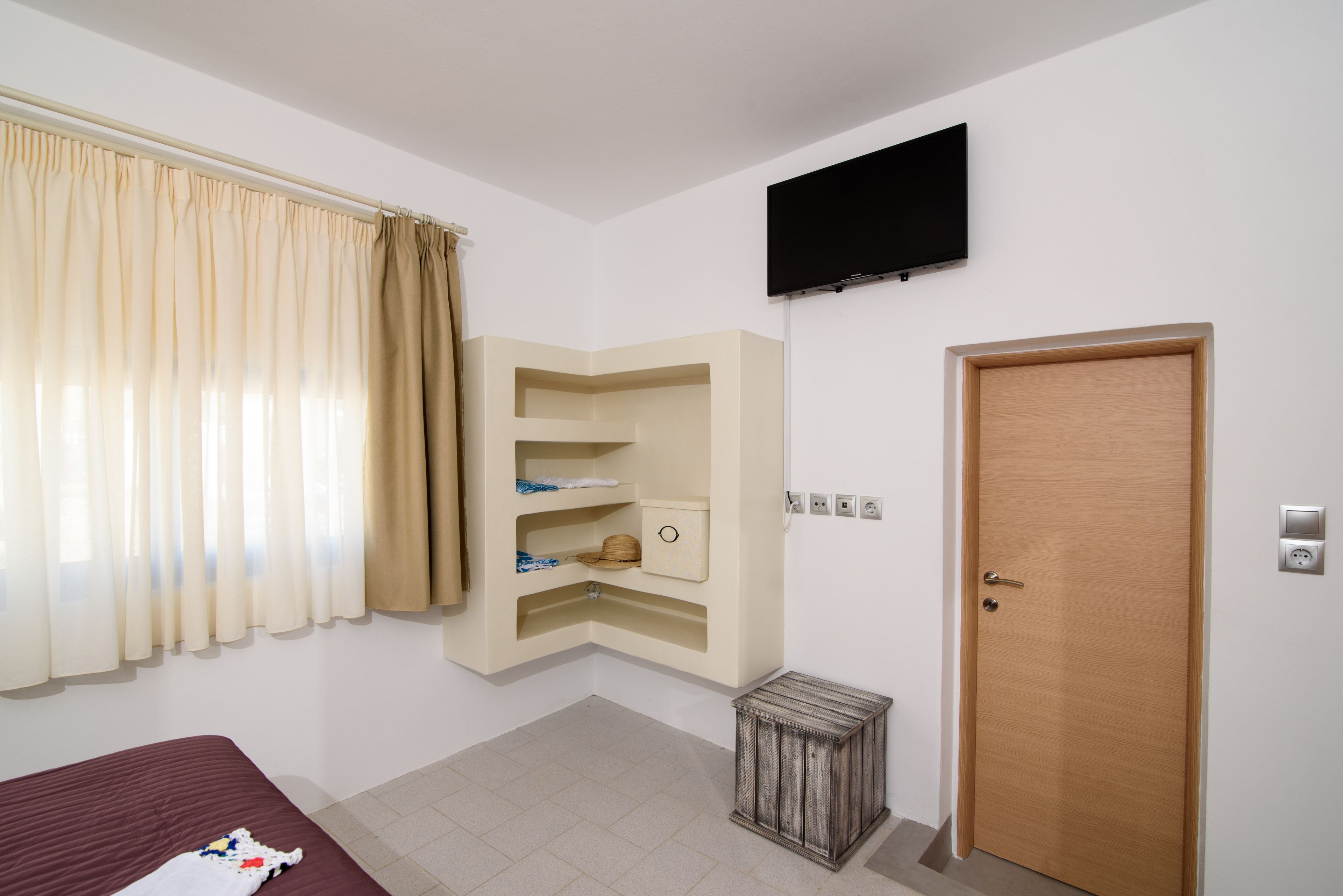 Une chambre d’hôtel avec un lit, un téléviseur fixé au mur, une porte en bois et une petite poubelle.