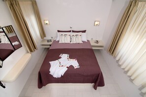 A neatly arranged bedroom with a large bed, two bedside tables, a bedside lamp, and a mirror on the left wall. - Villa George Santorini (Santorini)