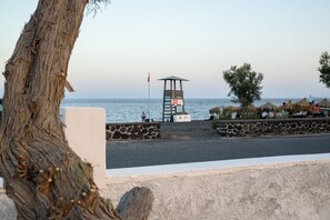 A beach with a lifeguard tower, stone walls, and a view of the sea. - Villa George Santorini (Santorini)