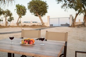A wooden table with two chairs, a plate of fruit, and two glasses of red wine. - Villa George Santorini (Santorini)