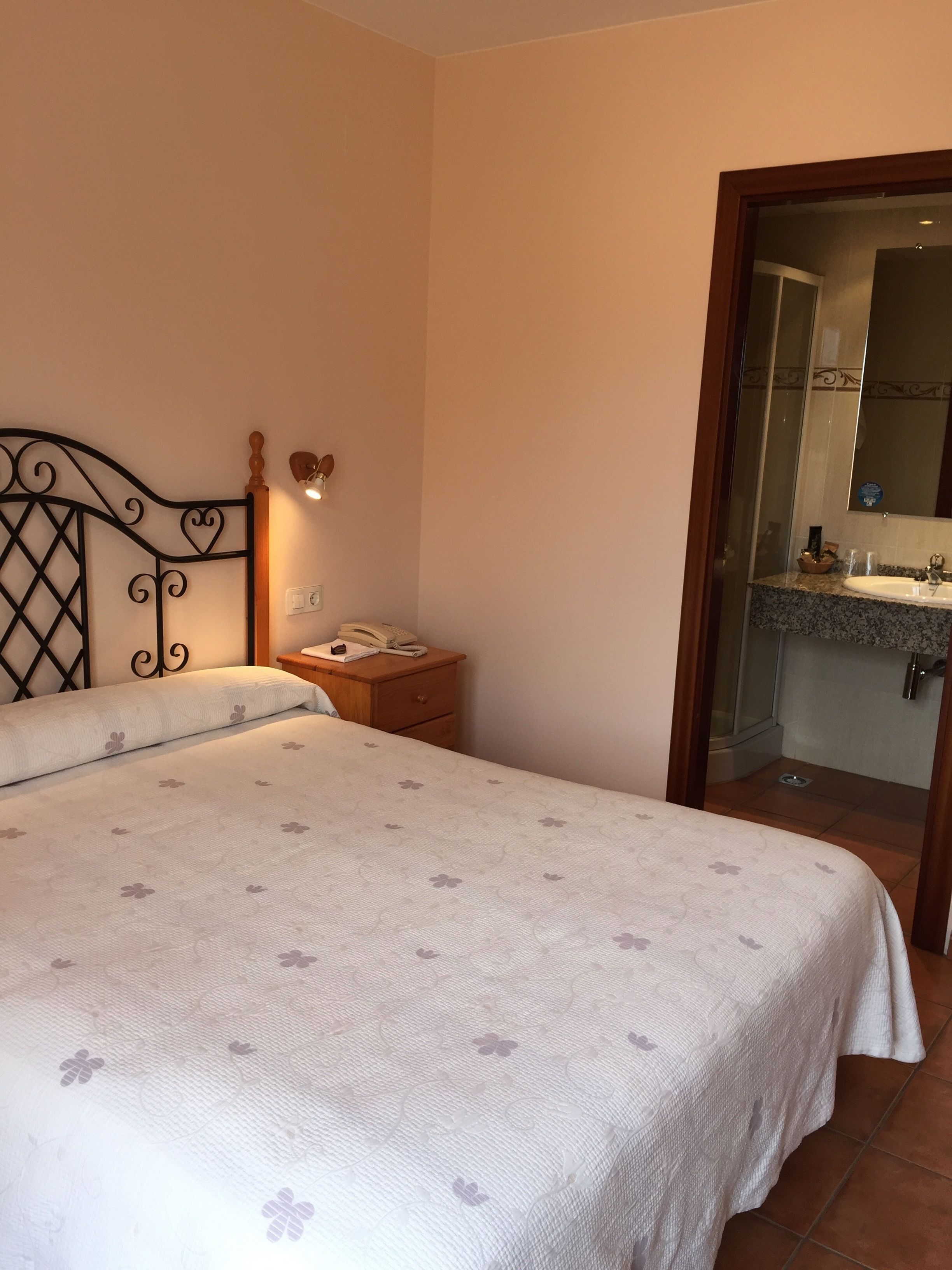 A bedroom with a bed, a nightstand, a bedside lamp, and a bathroom visible through an open door.
