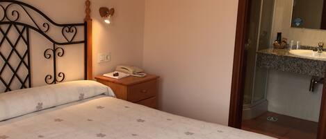 A bedroom with a bed, a nightstand, a bedside lamp, and a bathroom visible through an open door.