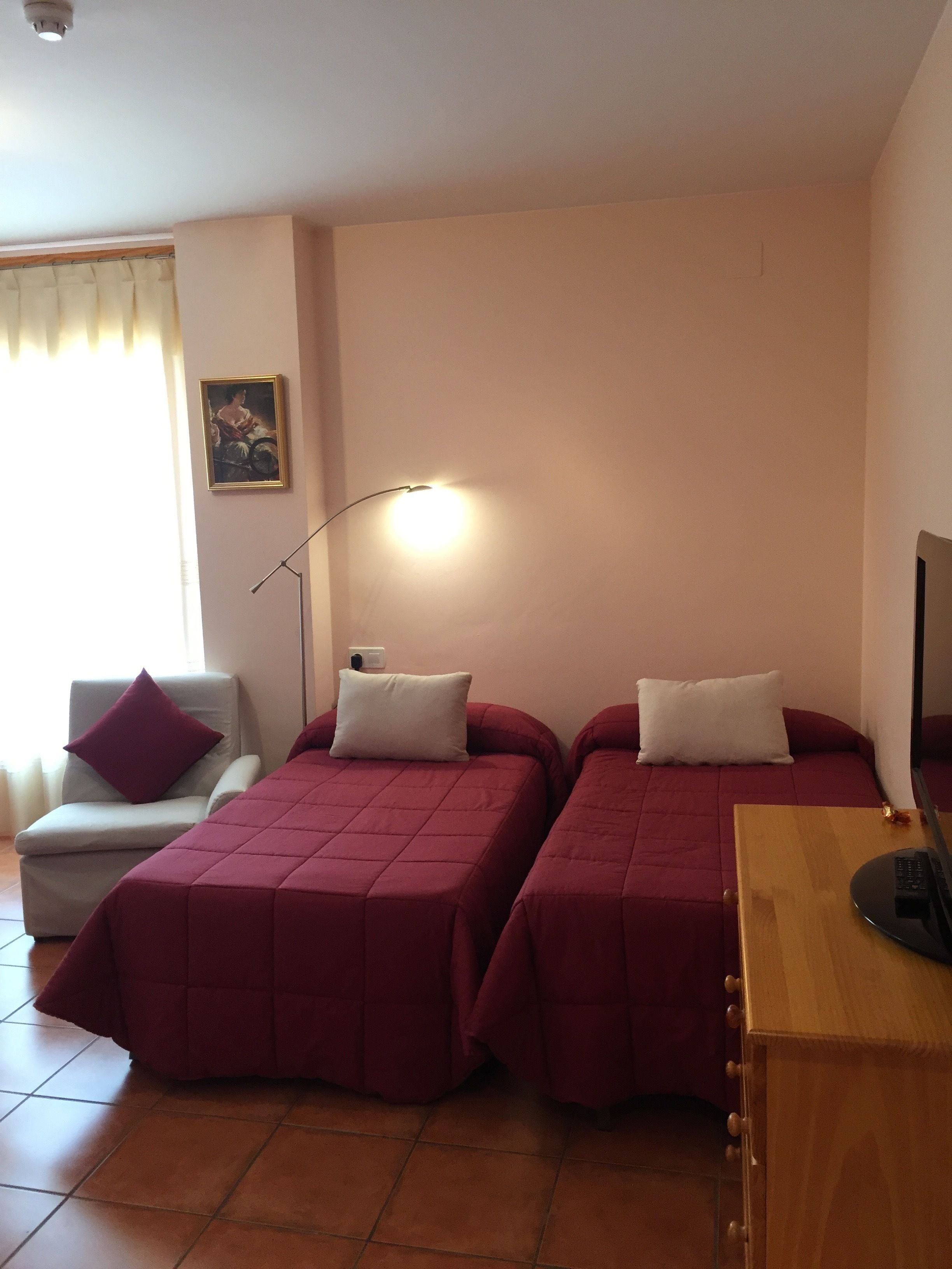 Una habitación con dos camas, una silla, un escritorio, una lámpara y un cuadro en la pared.