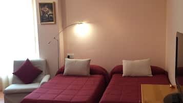 Una habitación con dos camas, una silla, un escritorio, una lámpara y un cuadro en la pared.