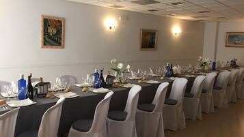 A long dining table set with chairs, wine bottles, and glasses in a well-lit room with ceiling lights and wall-mounted lamps.