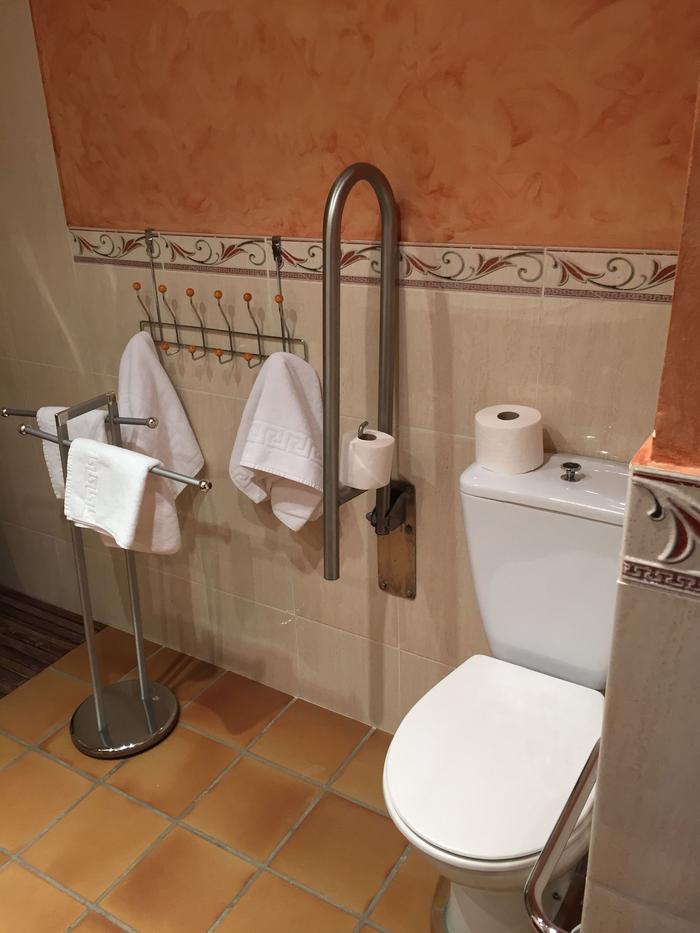 Un bagno con il water, un portasciugamani con diversi asciugamani e un dispenser per carta assorbente.