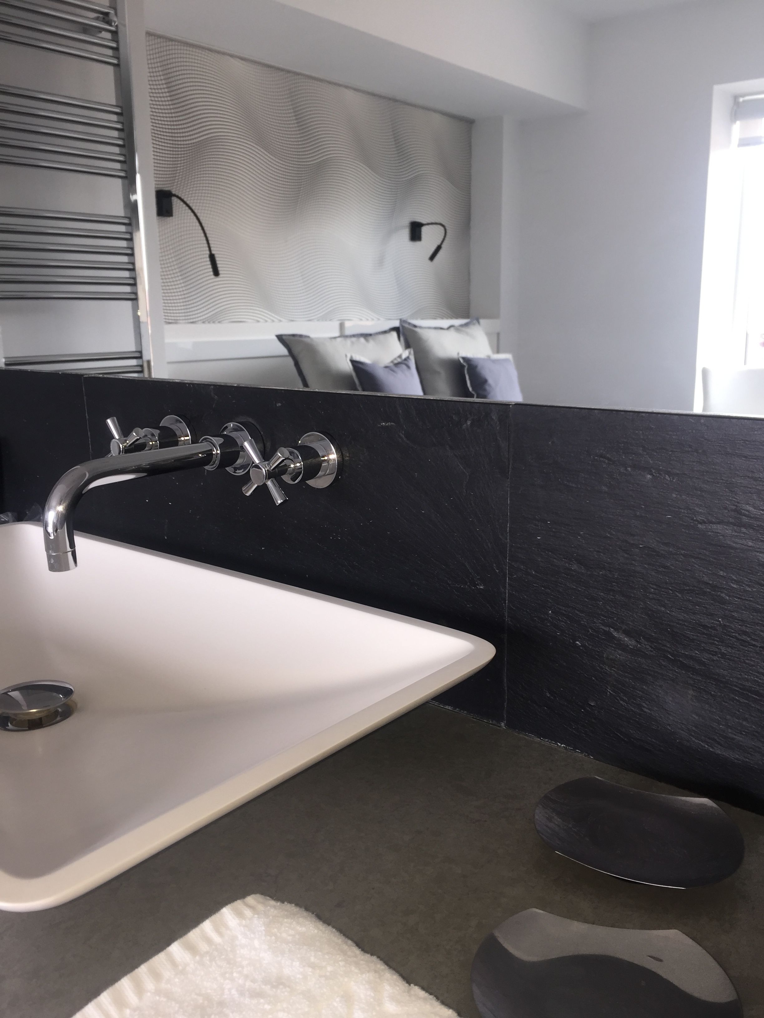 Un baño moderno con lavamanos blanco, salpicadero de mármol negro y un perchero para toallas.