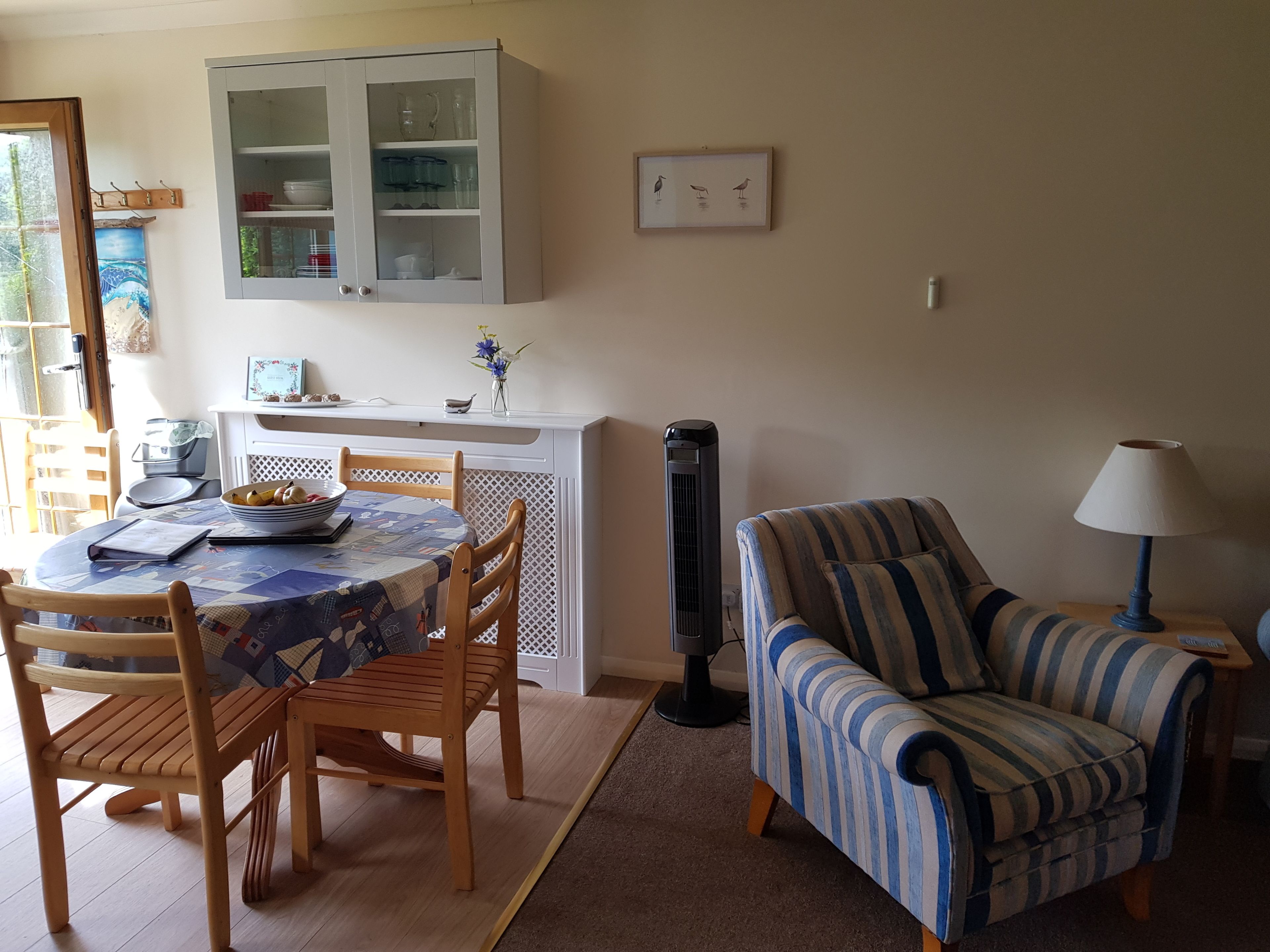 A dining area with a round table, chairs, a cabinet with glass doors, a wall-mounted picture, and a standing heater.