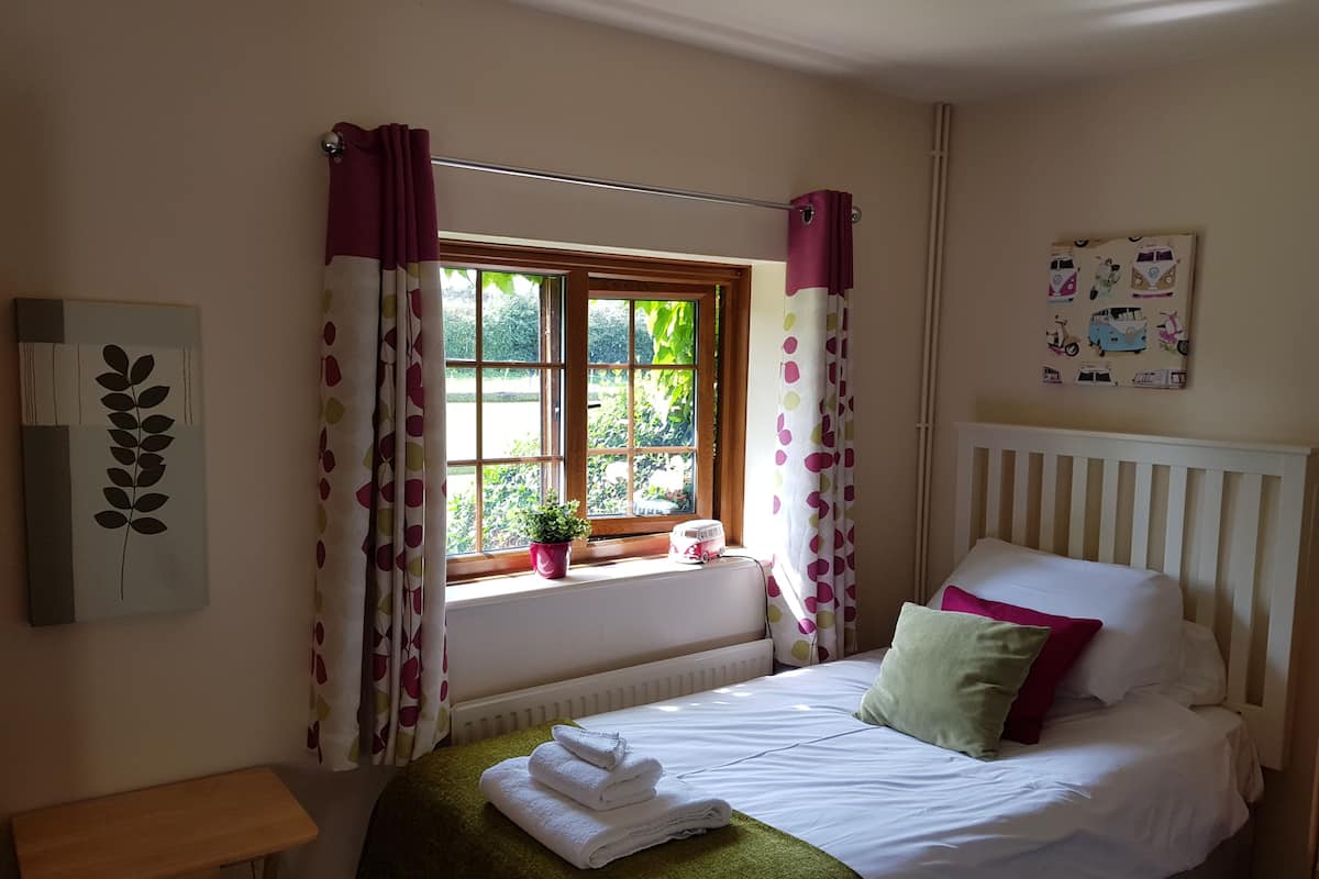Een slaapkamer met een bed, een raam met gordijnen, een radiator, een klein tafeltje en een wanddecoratie.