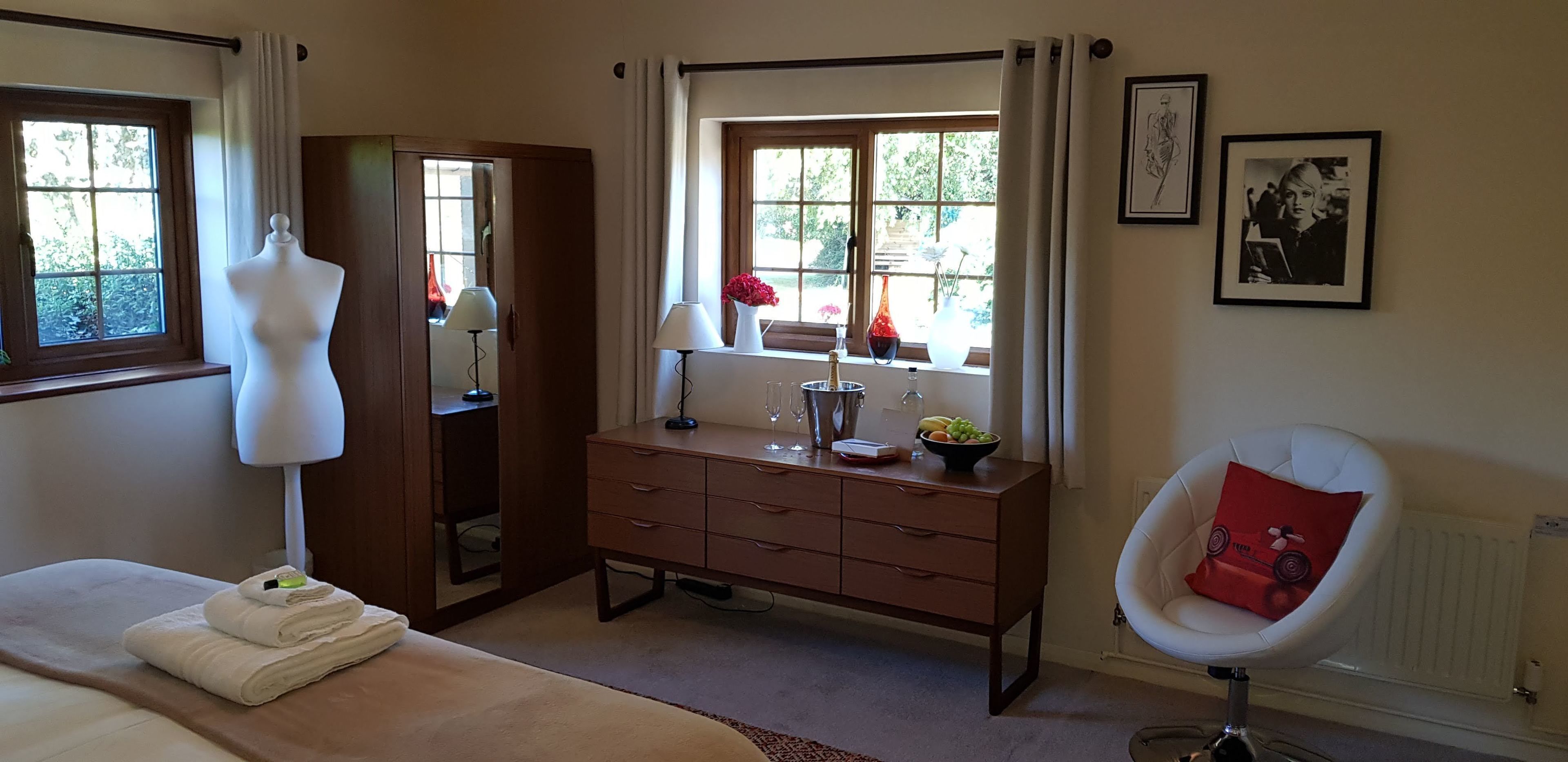 A bedroom with a bed, a dresser, a vanity, a chair, and a window with curtains.