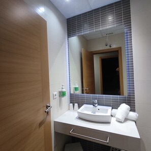 Un baño con lavamanos blanco, espejo y toallero.