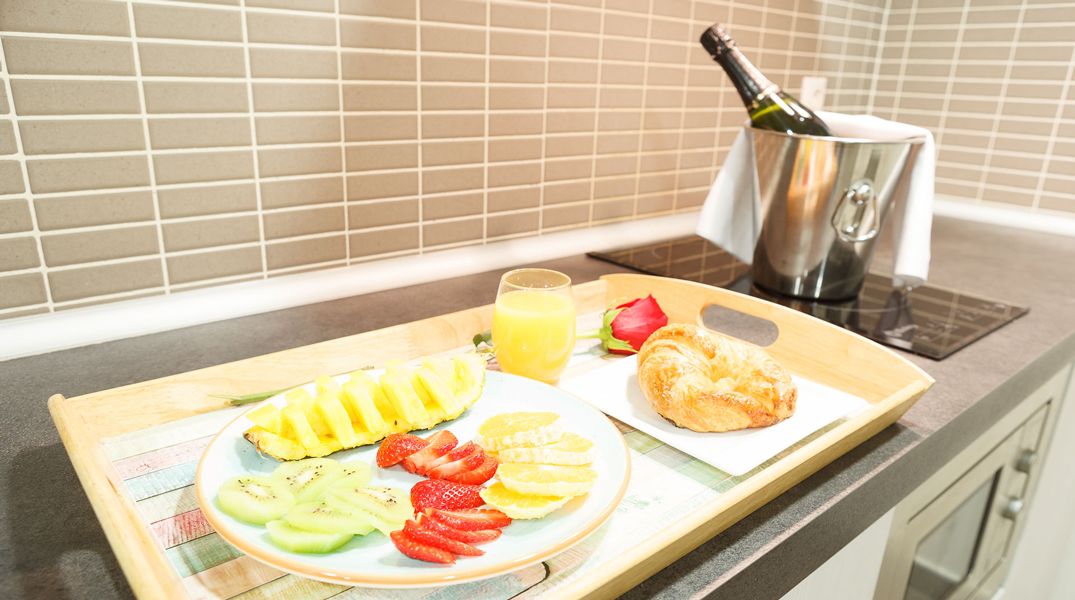 Ett frukostbricka med frukt, juice och en croissant, serverat på en träbricka.