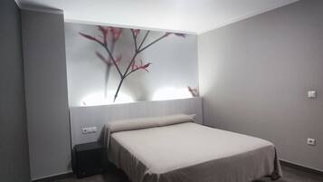 Quarto com cama, mesa de cabeceira, luminária na parede e janela com planta.