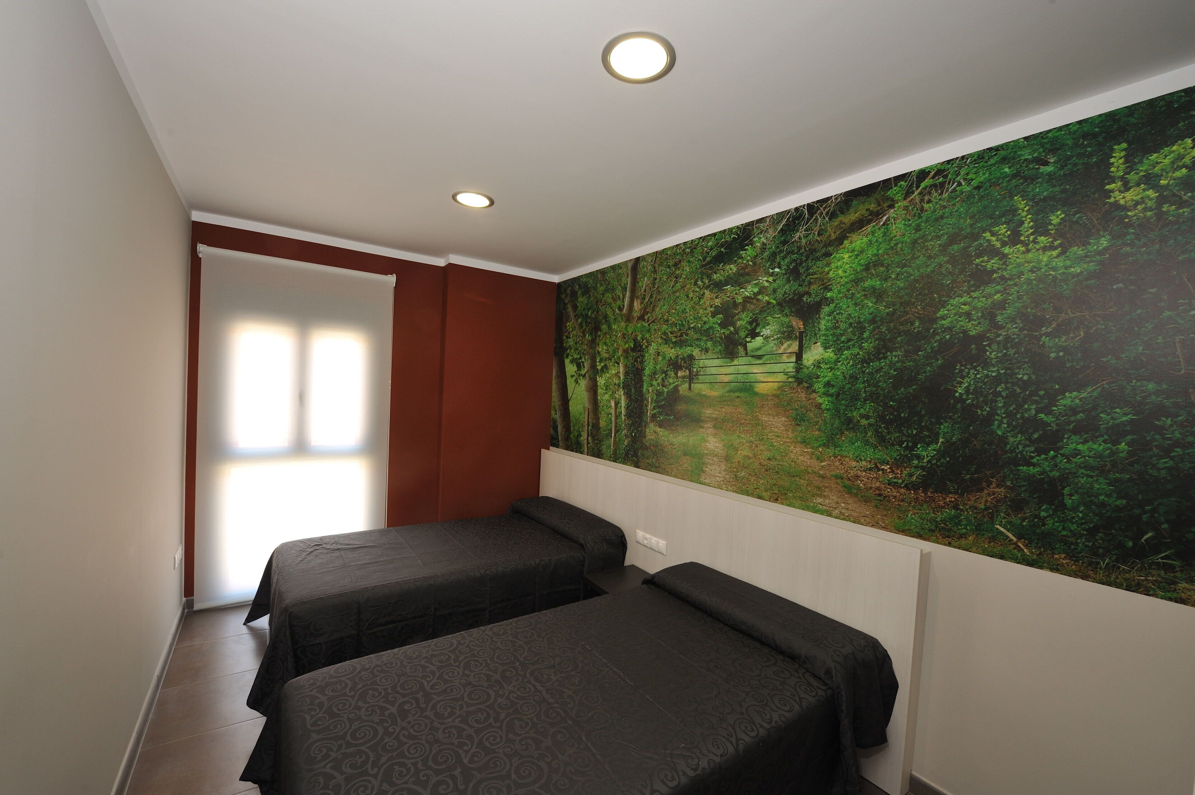 Una habitación con dos camas, un gran mural de un bosque en la pared y una ventana con persianas.