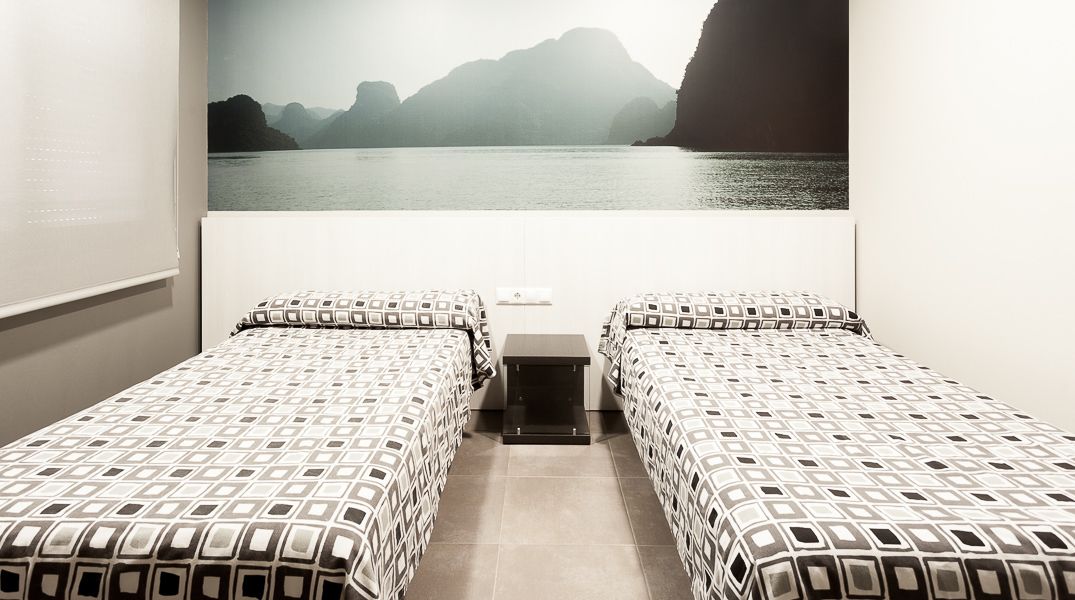 Een kamer met twee bedden, een tafeltje en uitzicht op een waterpartij met bergen in de verte.