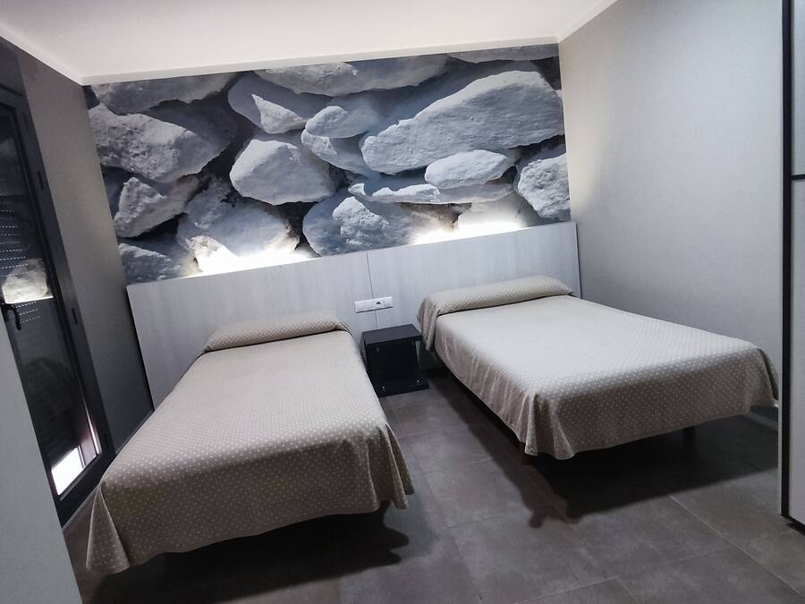A room with two beds, a stone wall, and a small table.