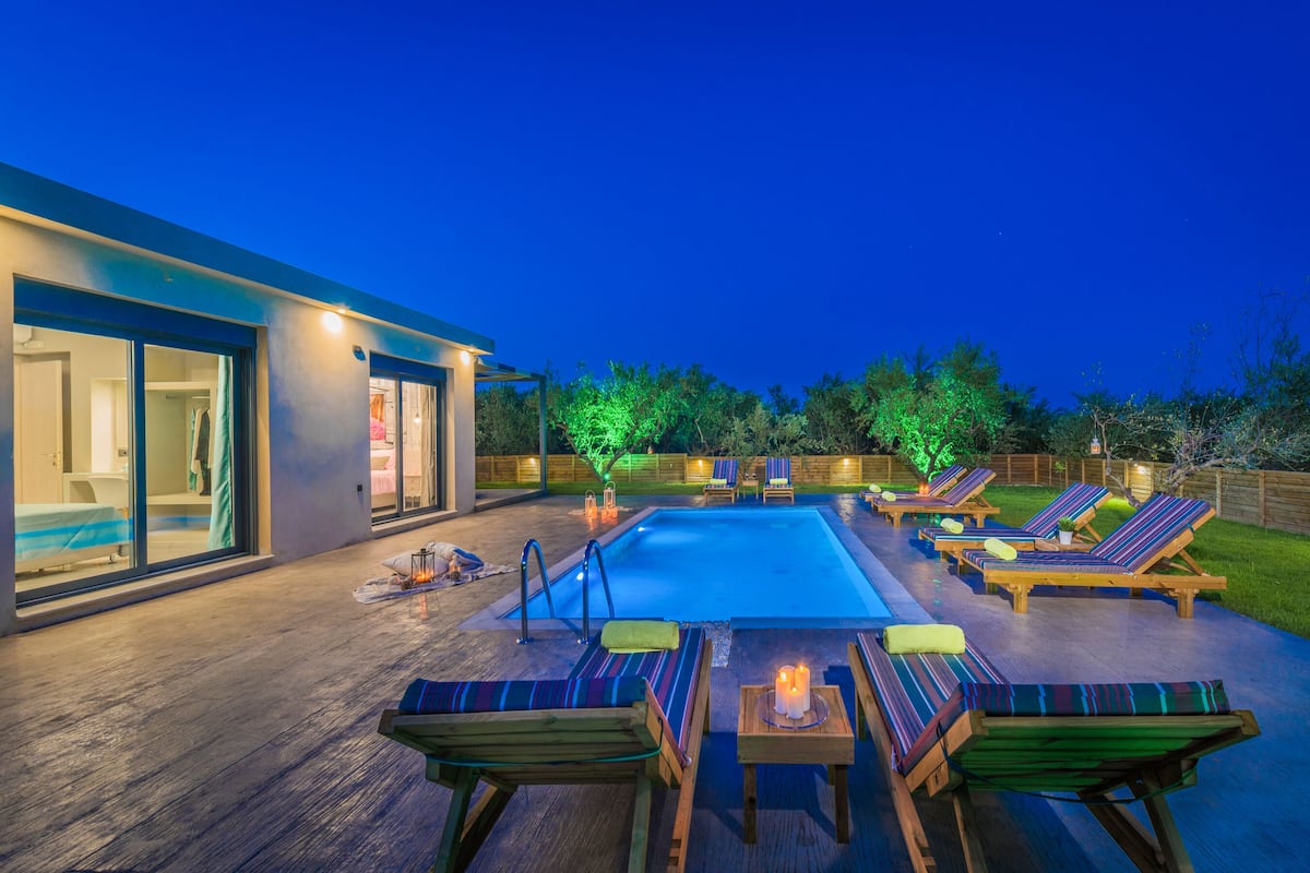 A modern house with a swimming pool, outdoor seating, and a well-lit patio area.