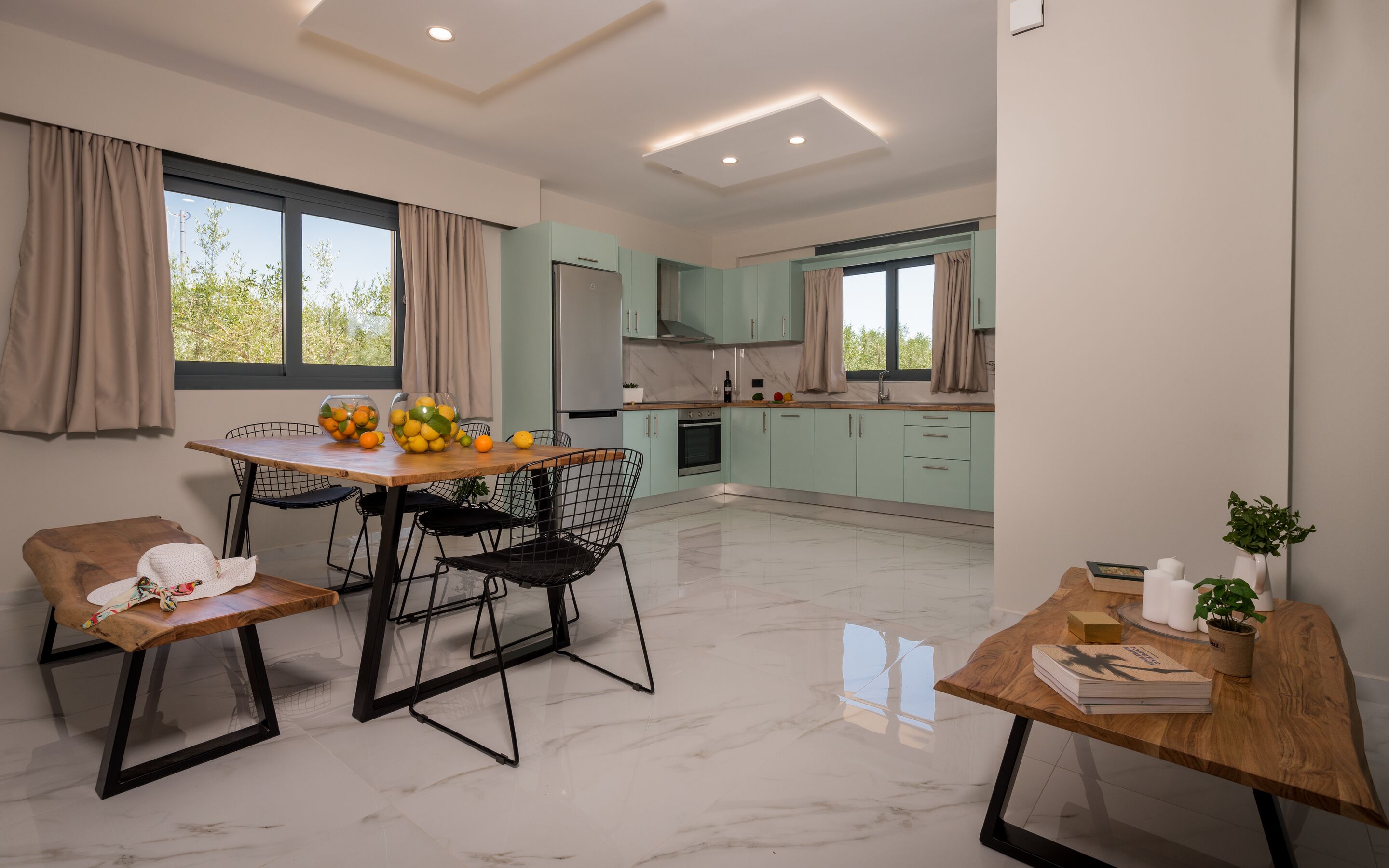 Une cuisine moderne avec des meubles de couleur vert clair, un plan de travail en marbre et un coin repas comprenant une table et des chaises en bois.