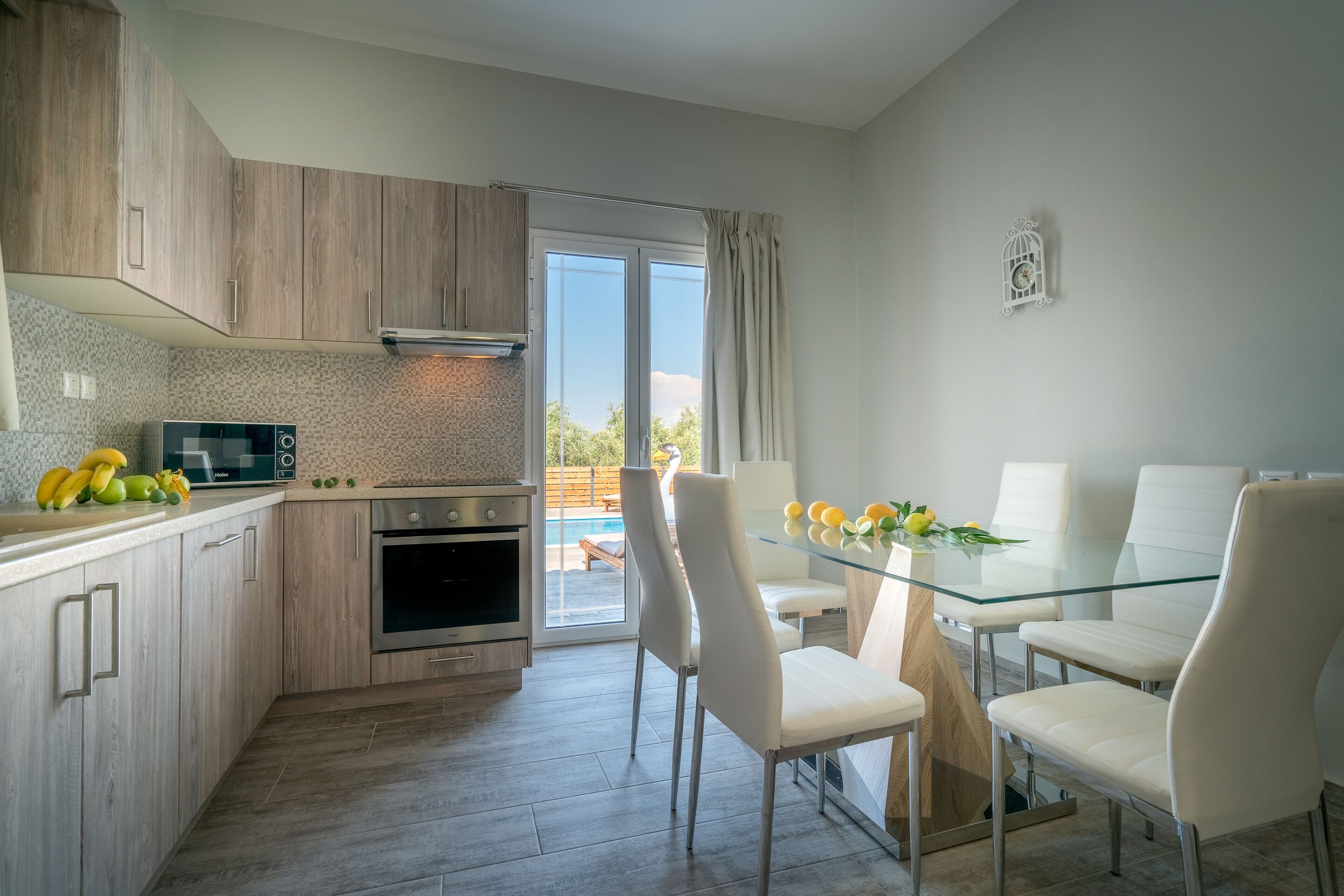 A modern kitchen with wooden cabinets, a glass dining table, and white chairs.