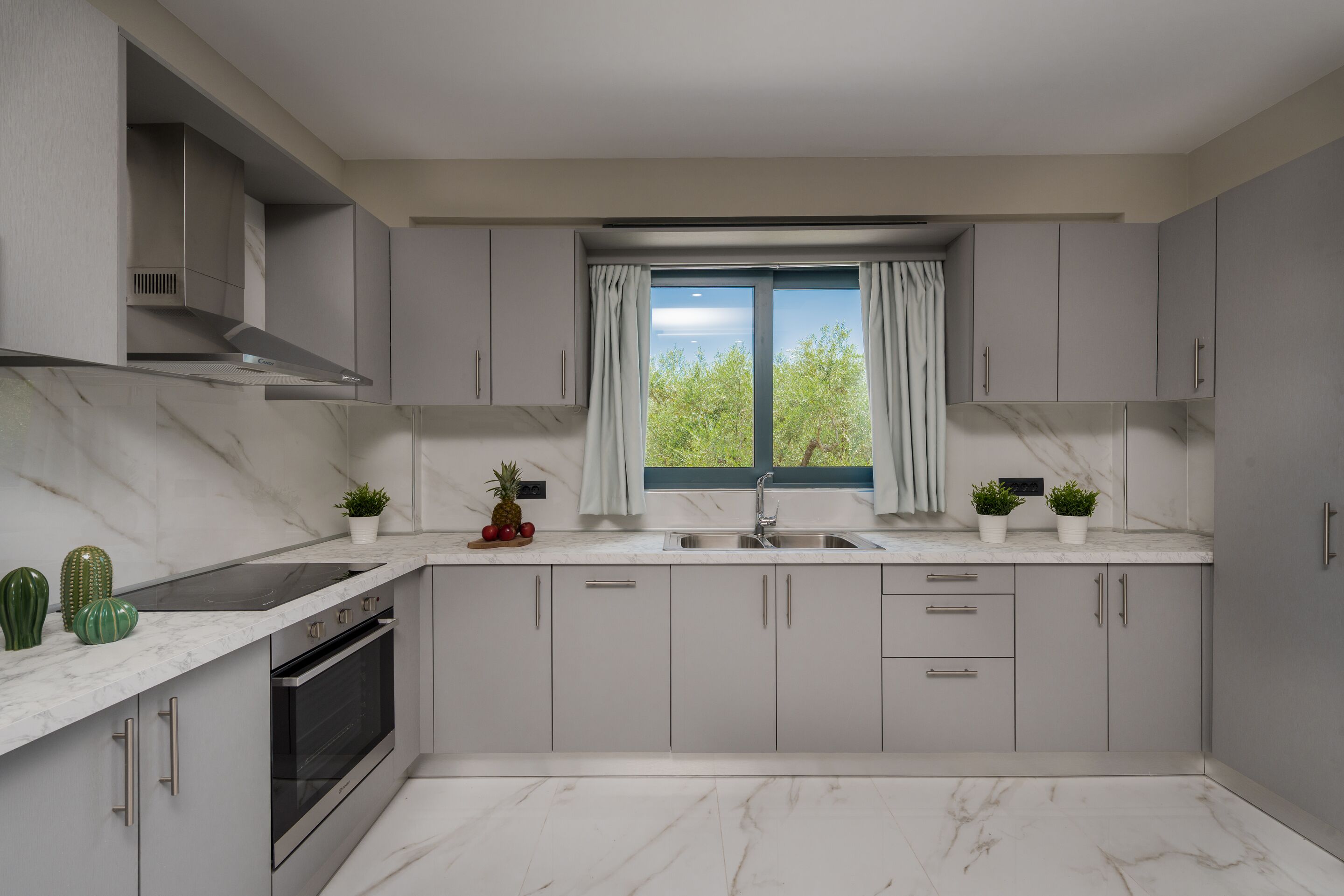 A modern kitchen with a built-in oven, stainless steel sink, and grey cabinets.
