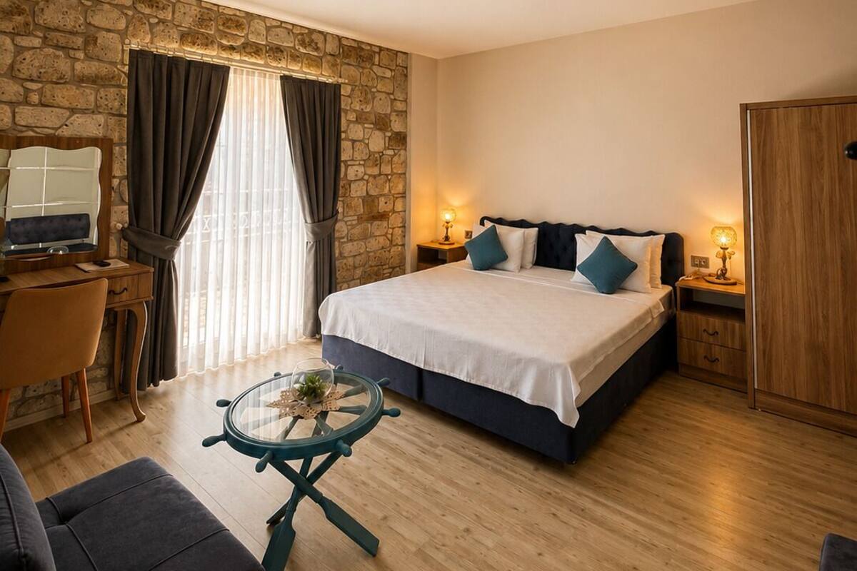 A bedroom with a stone wall, a bed with pillows, a desk with a computer, a chair, and a small table with a glass top.