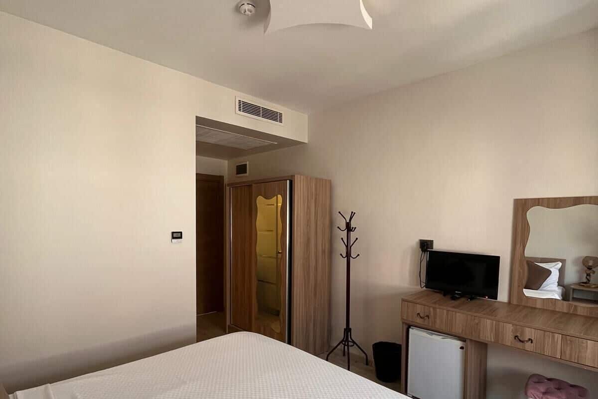 A hotel room with a bed, a desk, a chair, a television, and a coat rack.
