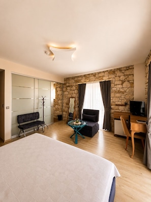 A hotel room with a bed, a desk, a chair, a sofa, a glass table, and a stone wall. - F&G Alaçatı (Cesme)