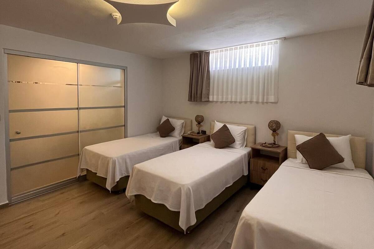 A hotel room with three single beds, a wardrobe, a bedside table with a lamp, and a ceiling light fixture.