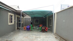 Een overdekt terras met een tafel, stoelen, een duwdeur en een bordje dat 24-uurs bediening aangeeft.