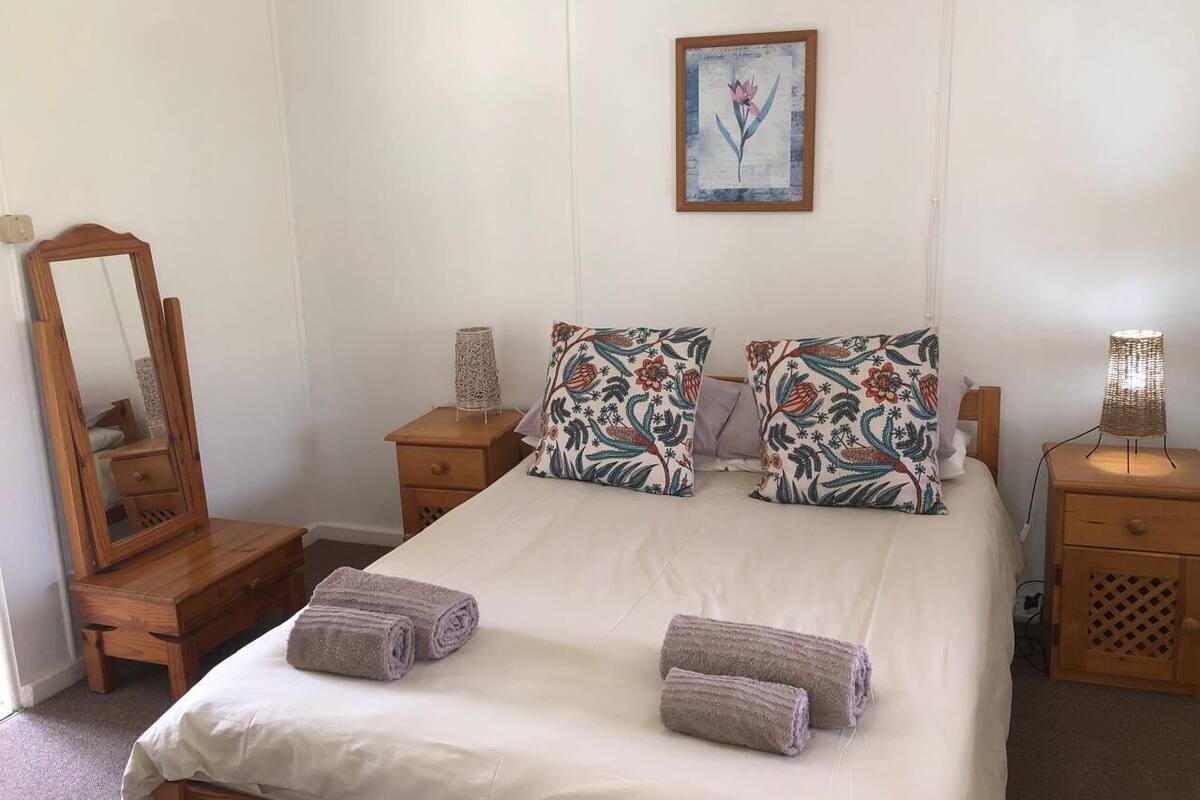 A bedroom with a bed, two nightstands, a wooden dresser, a mirror, and a floral-patterned pillow.