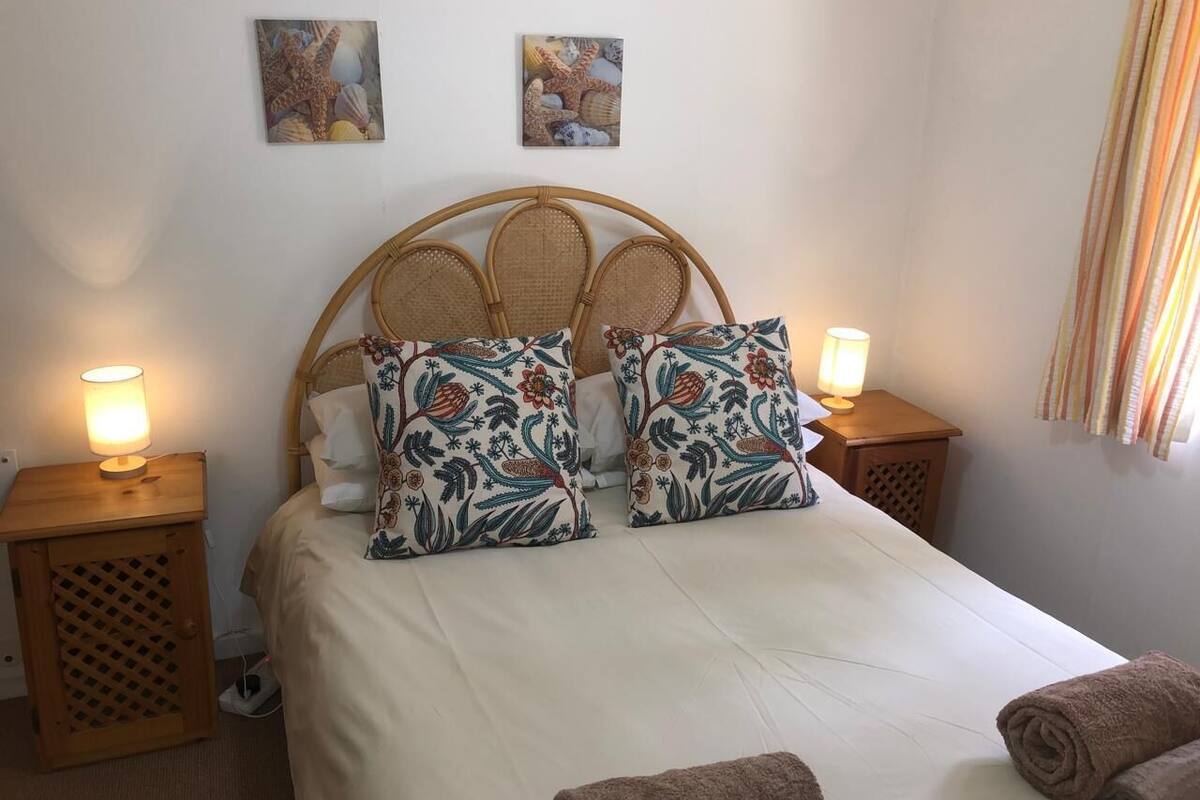 A bed with a woven headboard, two matching pillows, two bedside lamps, and a pair of towels on the floor.