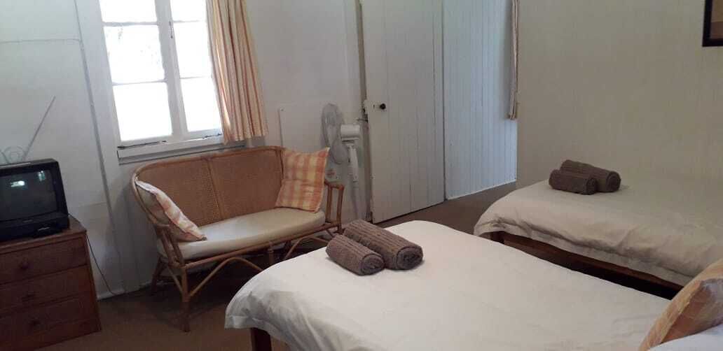 Quarto com duas camas, uma cadeira, televisão e janela com cortinas.