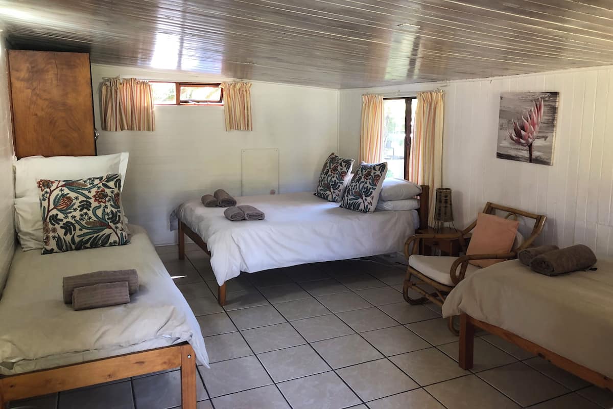 A room with three beds, a wooden wardrobe, a chair, and a painting on the wall.
