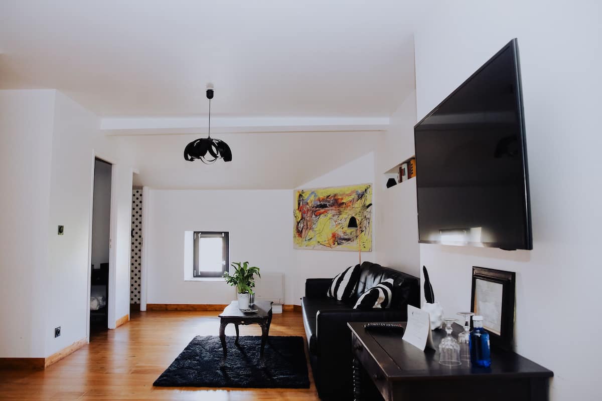A modern living room with a black leather sofa, a coffee table, a black rug, a flat-screen TV, and a painting on the wall.