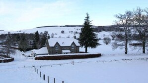 A snow-covered landscape with a stone building surrounded by trees and a fence. - Shian Cottage B&B (Dunkeld)