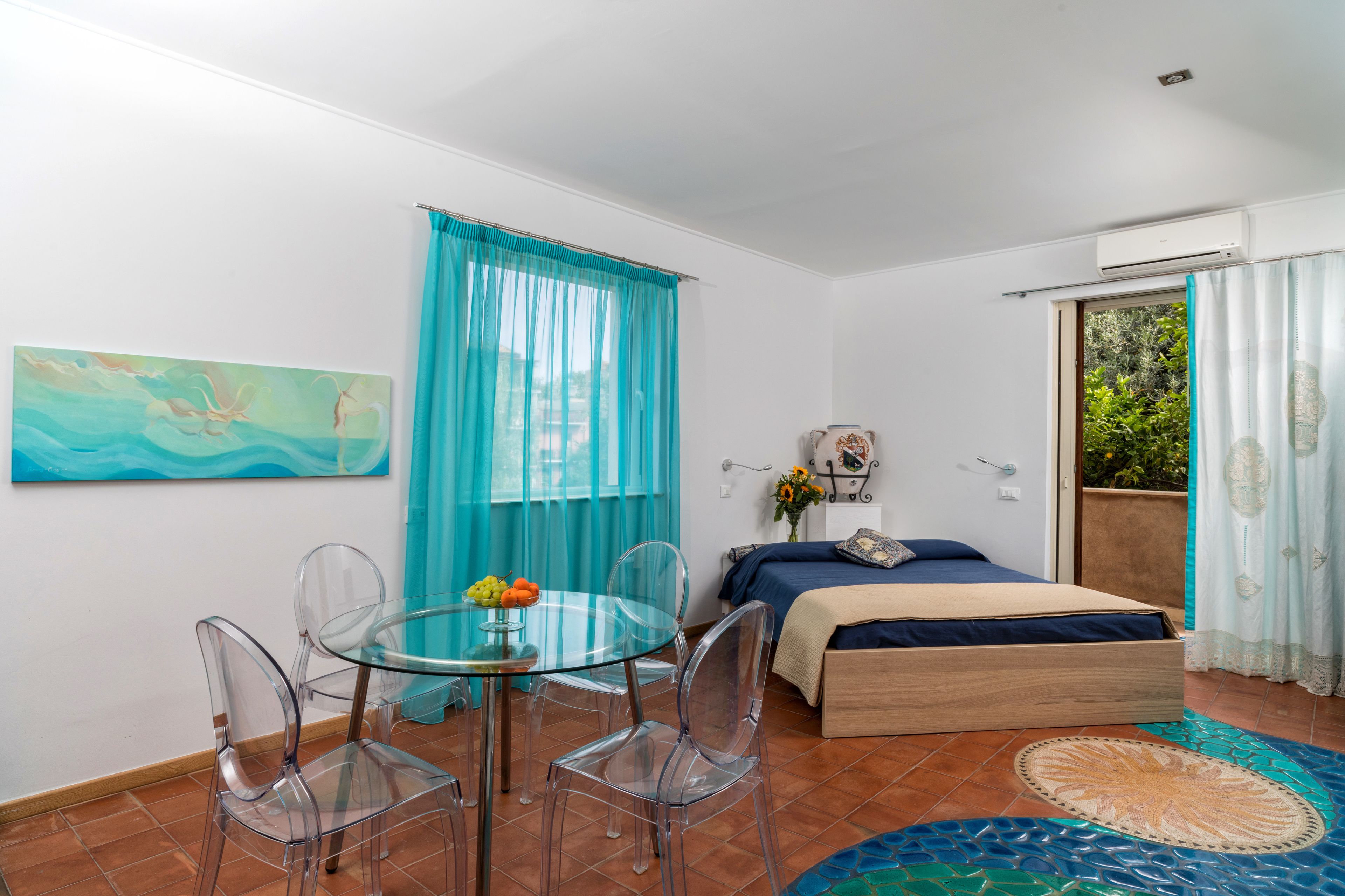 Ein Zimmer mit einem Bett, einem Glastisch mit Stühlen, einem Gemälde und Blick auf Grün.