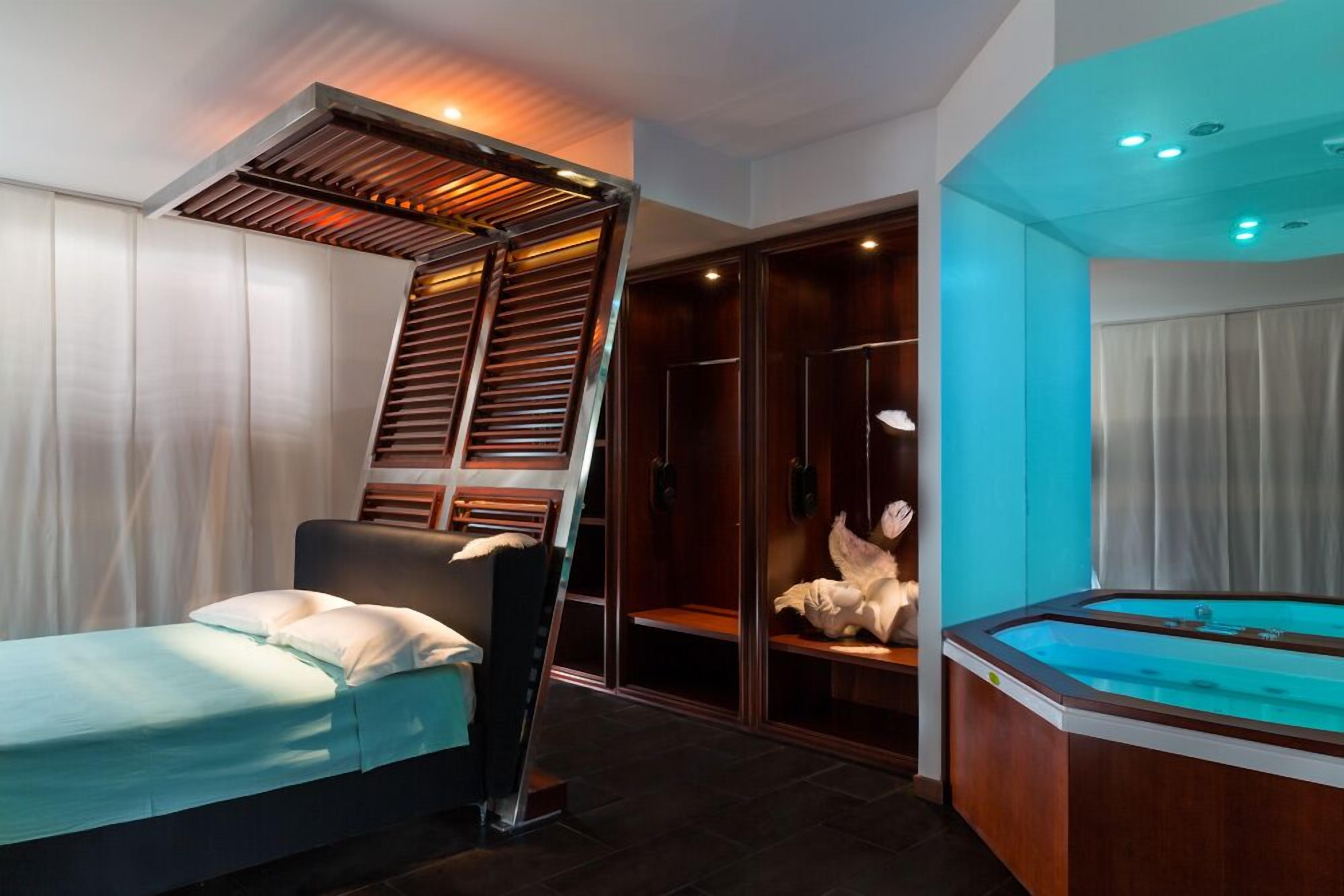A modern hotel room with a bed, a glass-enclosed jacuzzi, and a wooden ladder leading to a walk-in closet.