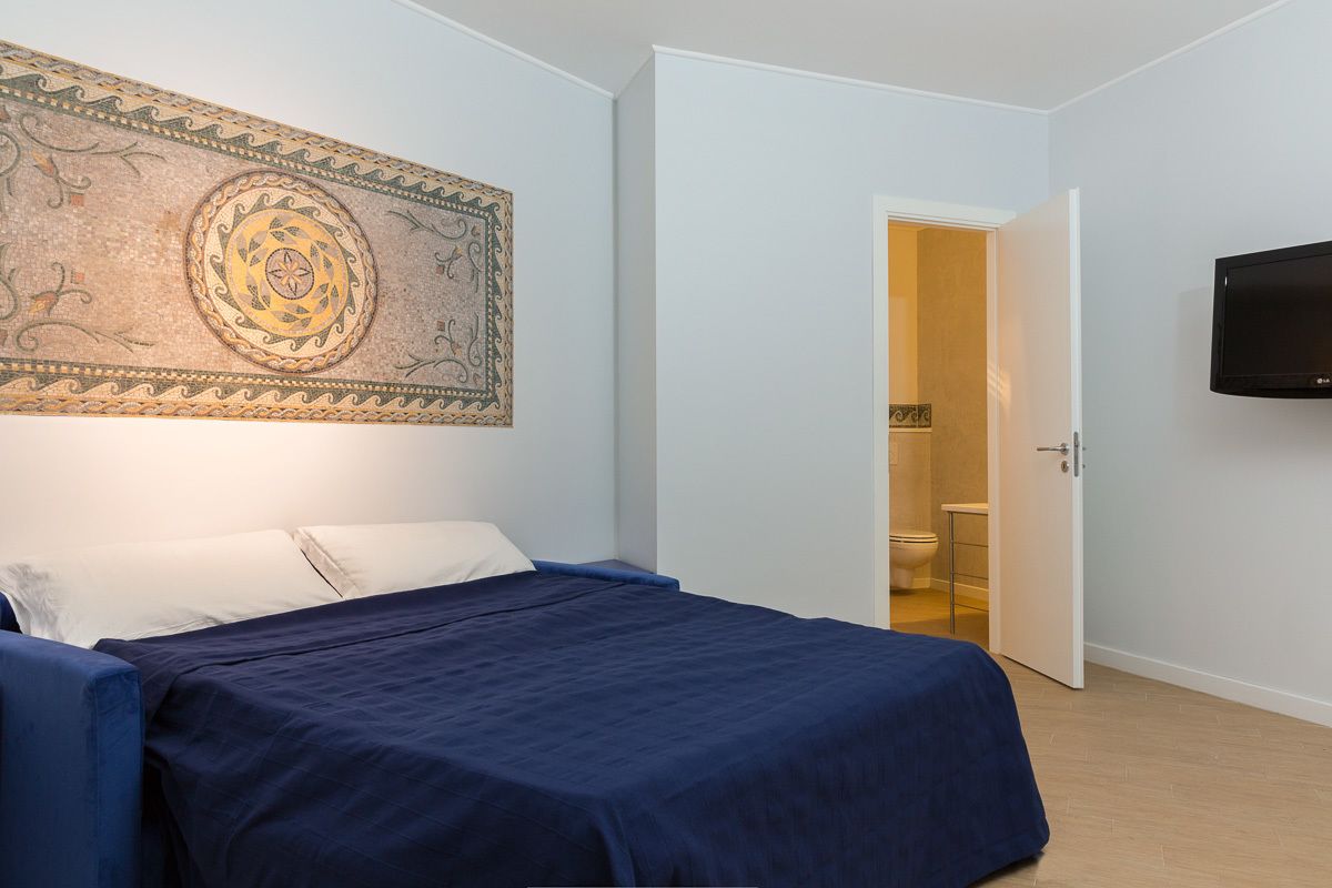 A bedroom with a bed, a television, and a bathroom visible through an open door.