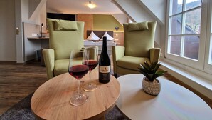 A modern living room with two green armchairs, a round wooden table with a bottle of red wine and two glasses, and a small potted plant. - Hotel-Gasthaus Goldener Engel (Glottertal)