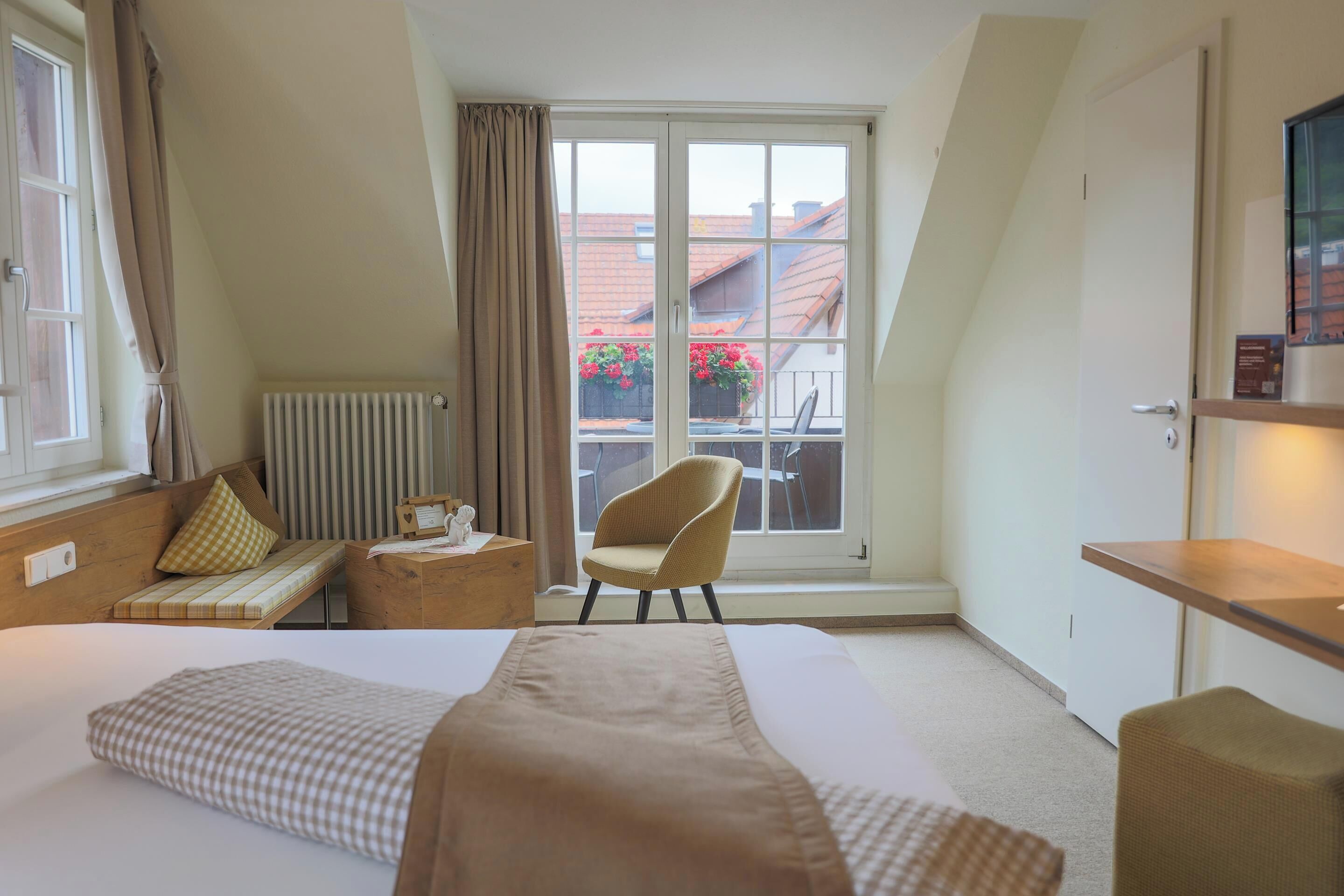 Een hotelkamer met een groot bed, een stoel, een kleine tafel en een raam met uitzicht op gebouwen en bloemen.