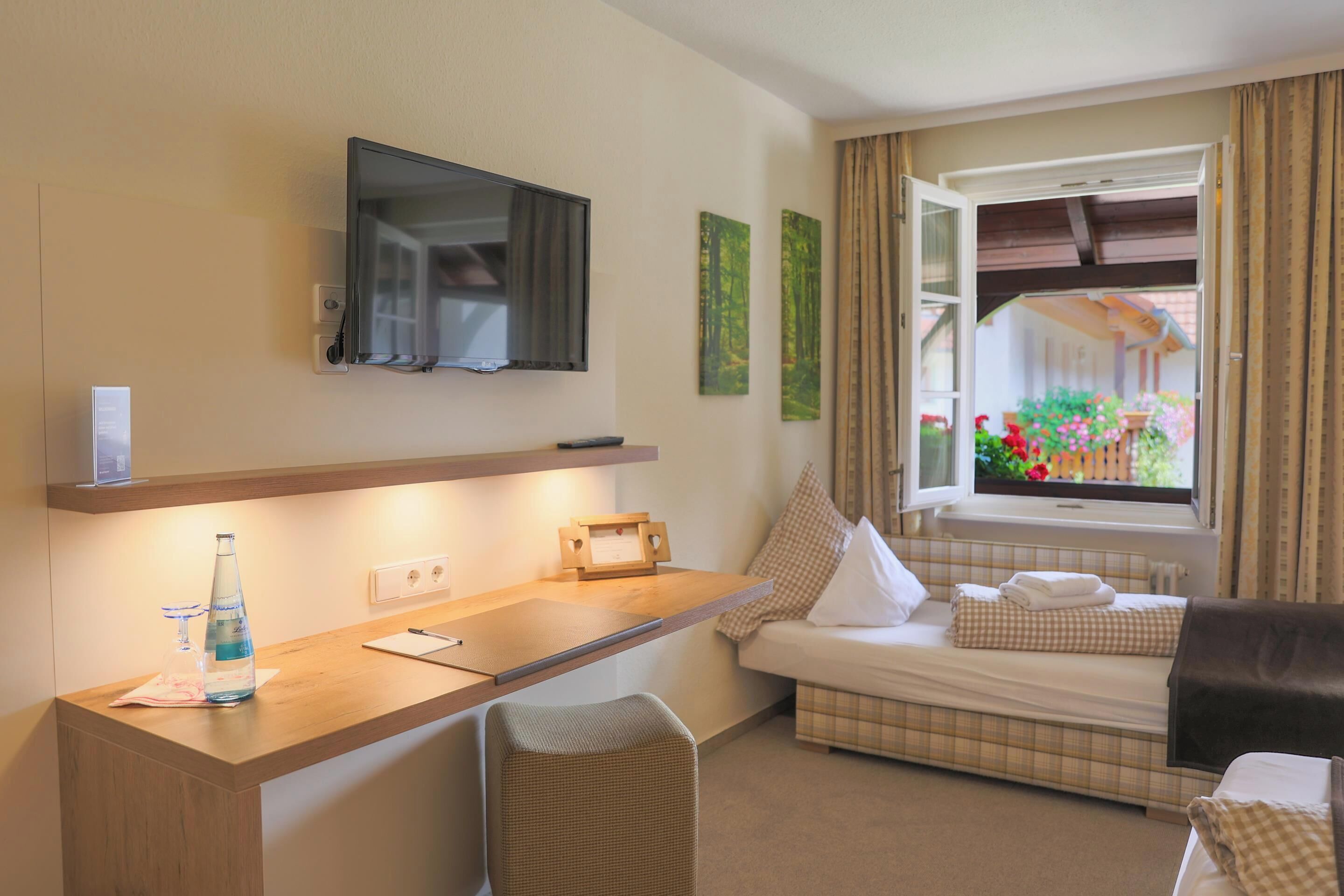 Ein Hotelzimmer mit Bett, Schreibtisch, Stuhl, Fernseher und einem Fenster mit Vorhängen.