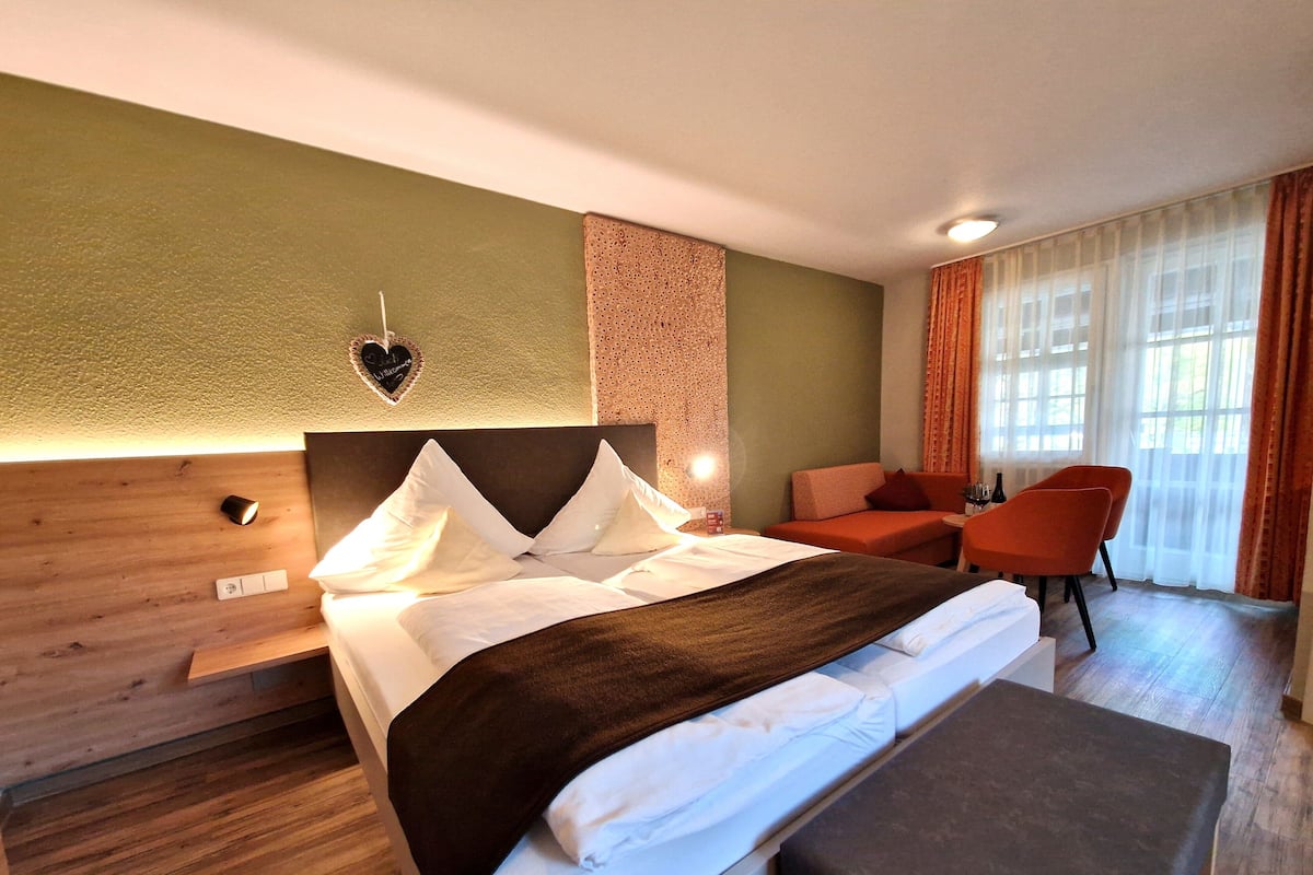 Ein Hotelzimmer mit einem Bett, einem Nachttisch, einem Sessel und einem Fenster mit Vorhängen.