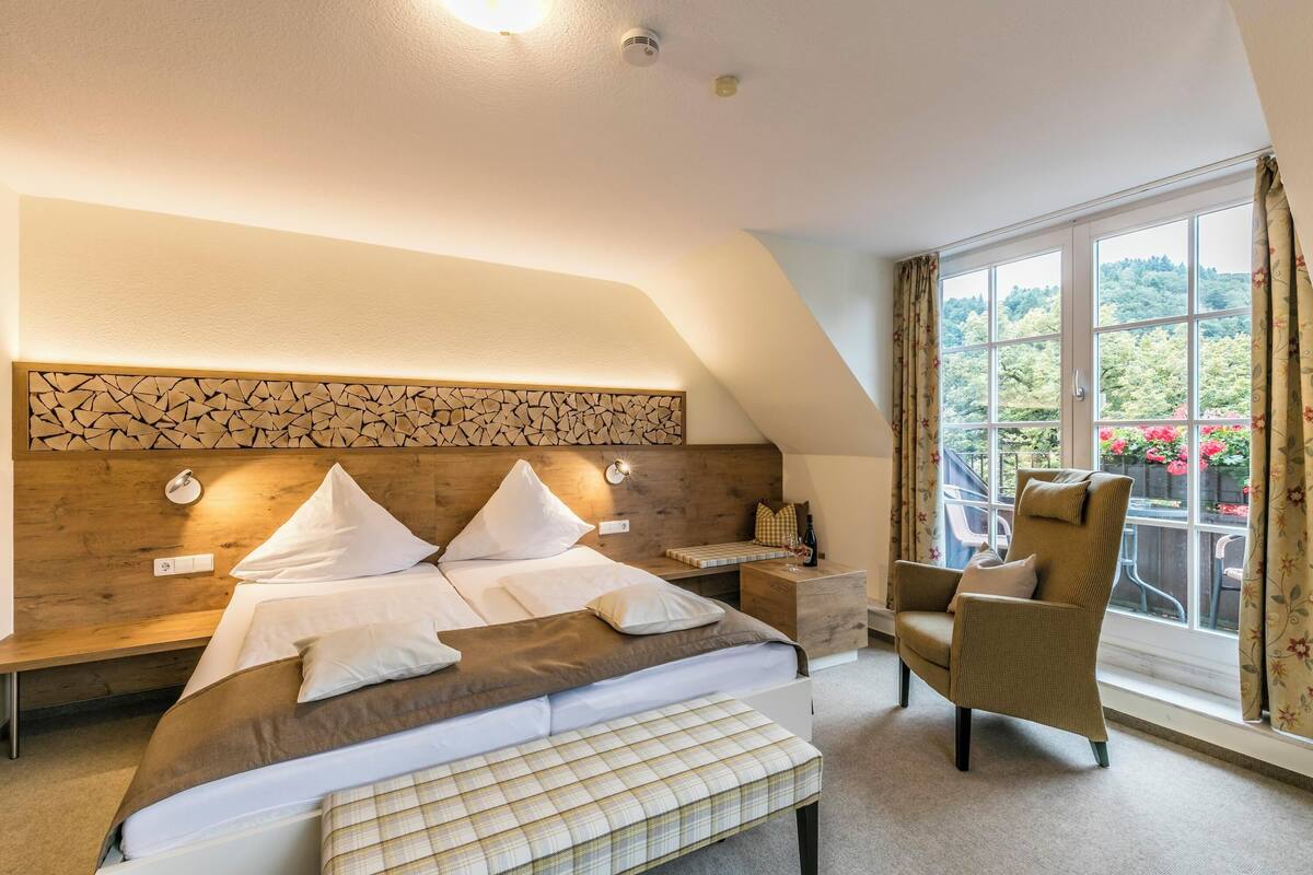 Ein Schlafzimmer mit einem großen Bett, einem hölzernen Kopfseitenverkleidung, einem Nachttisch, einem Sessel und einem Fenster mit Vorhängen.